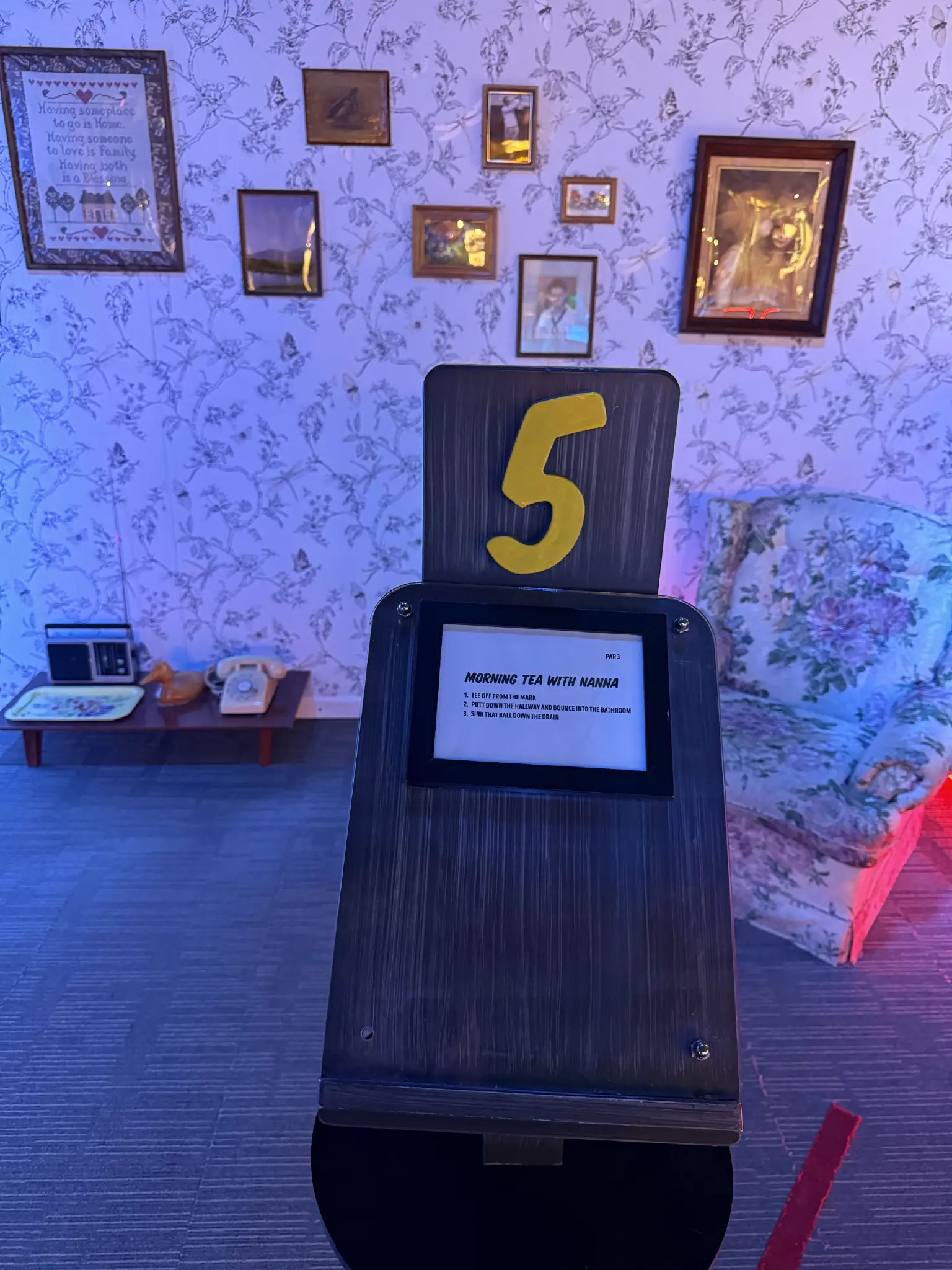 A putt putt hole that is set as an old granny’s living room, with flowered wall paper and matching chair. Old photos line the wall.
